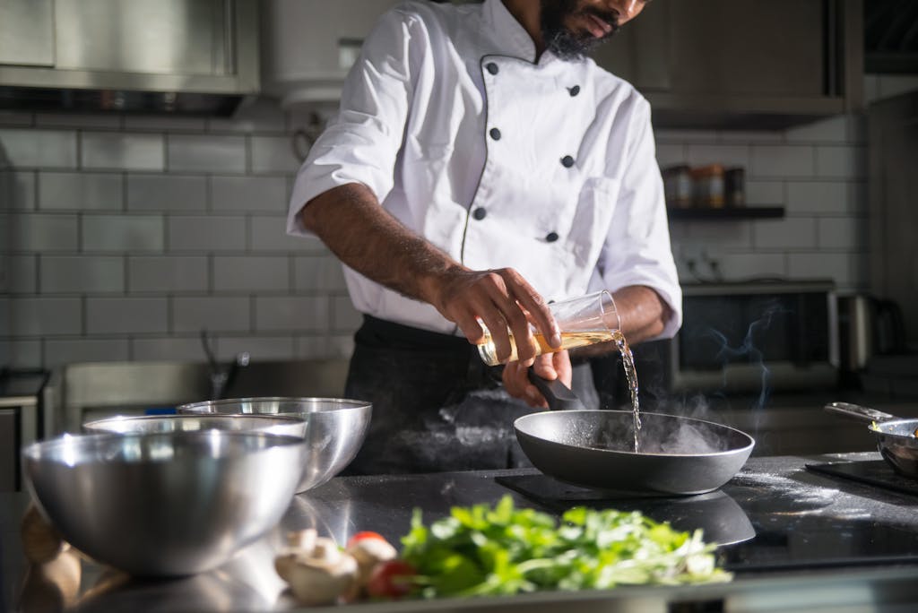 Chef in a professional kitchen pouring oil into a frying pan for cooking.